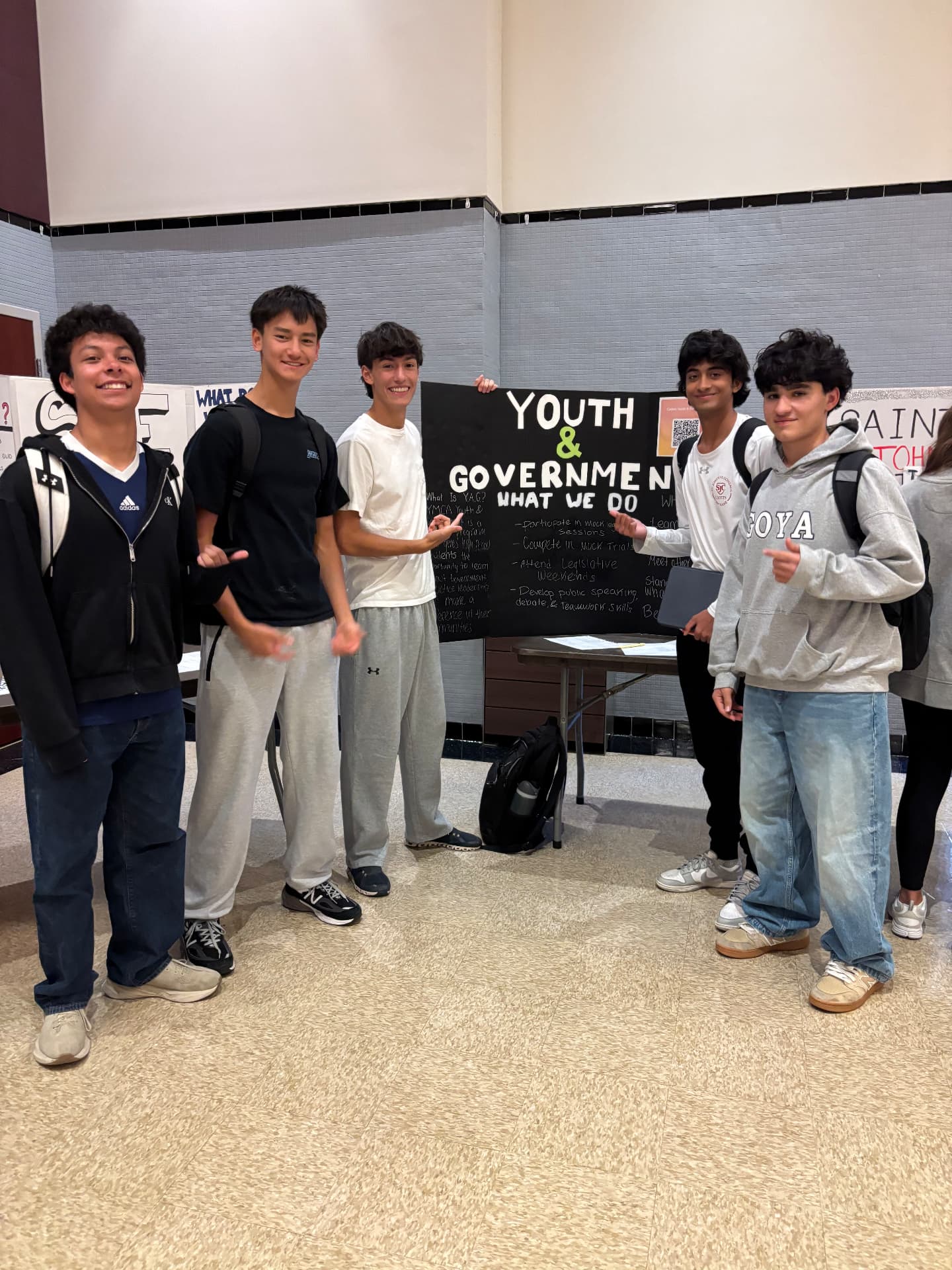 Five Youth & Government club members standing in a row beside their display board at a school activity fair